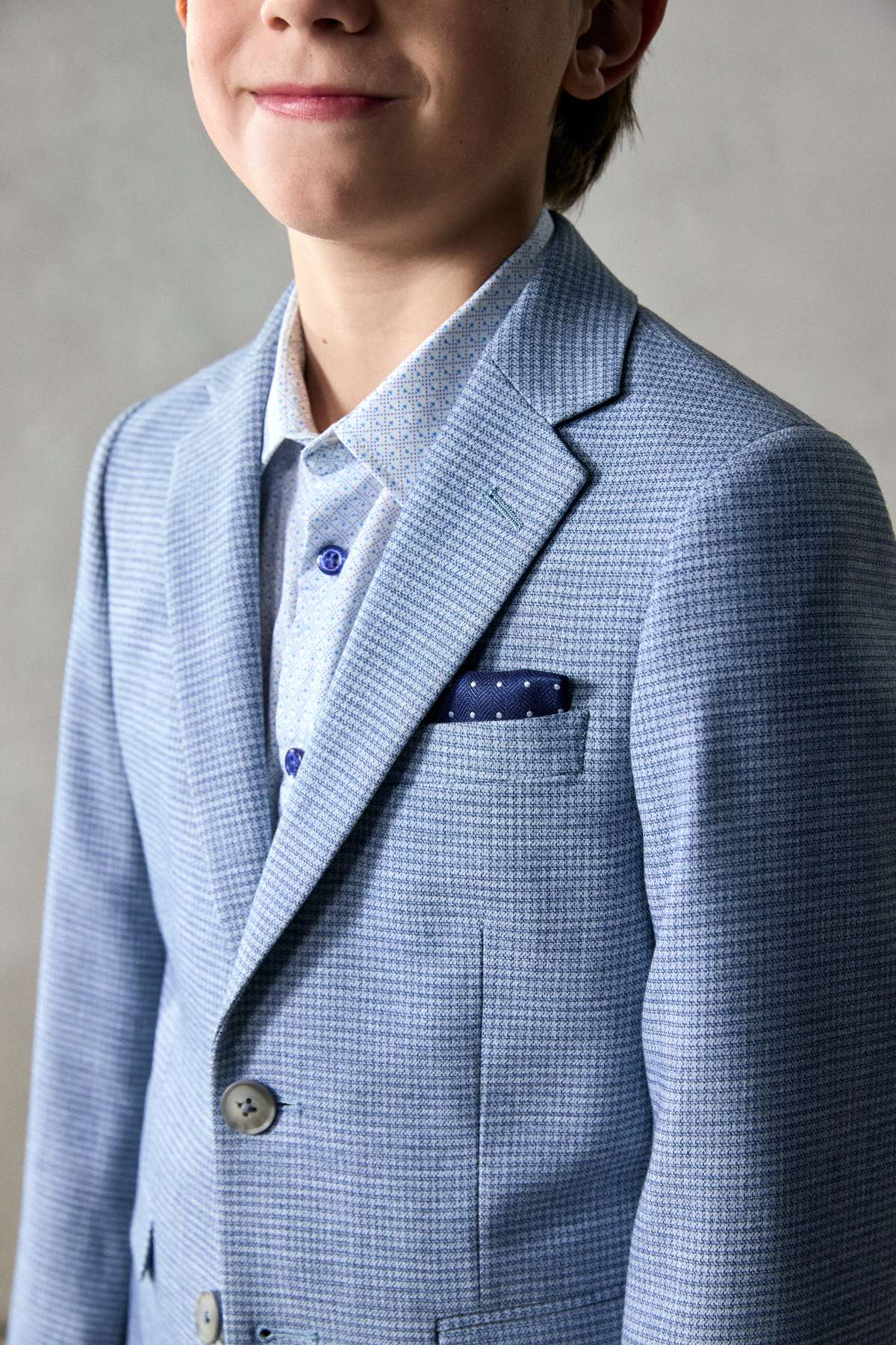 Child wearing a light blue checkered suit with a gray background