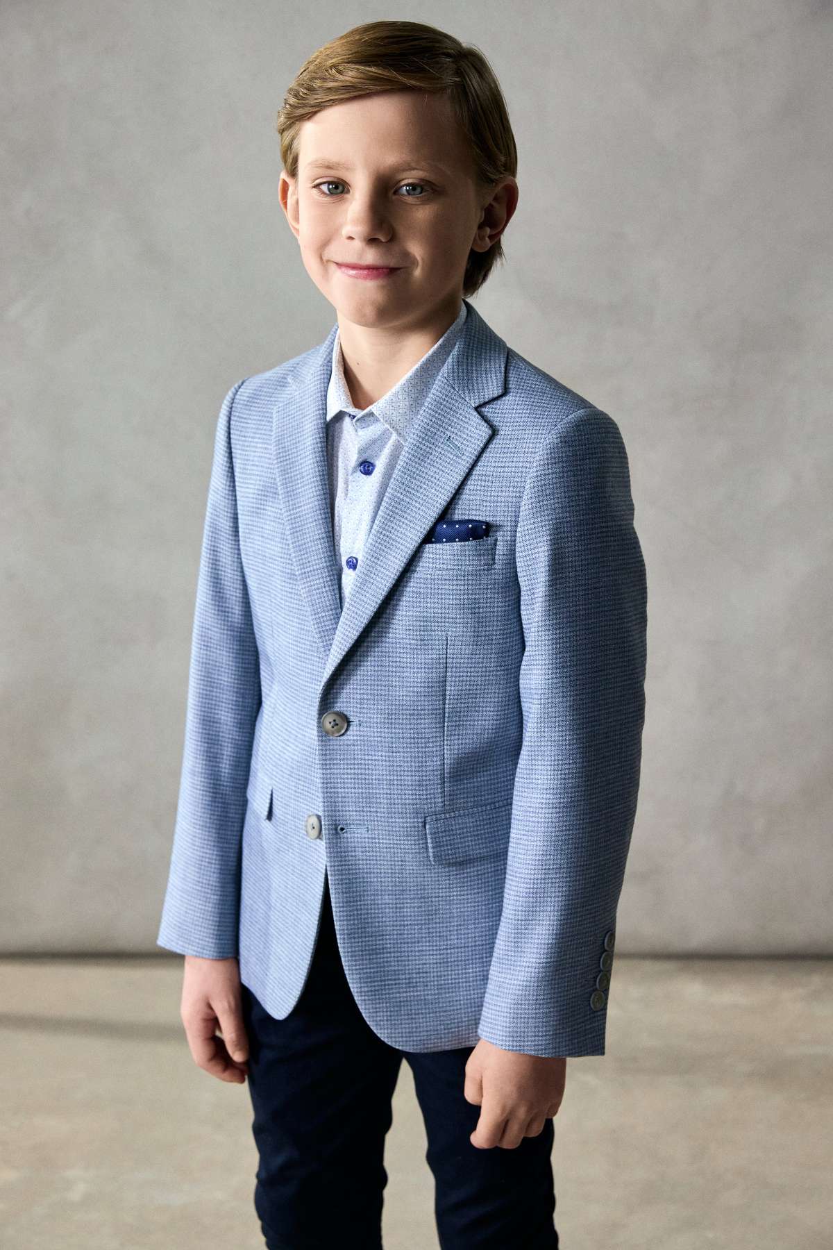 Young boy wearing a light blue blazer over a white shirt with a gray background