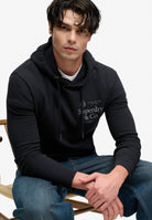 Superdry 1954 Company Relaxed Hoodie in Dark Navy seated model view