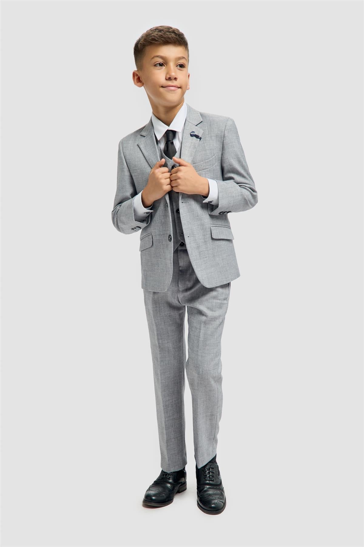 Young boy wearing a gray suit with a white shirt and black shoes on a light gray background
