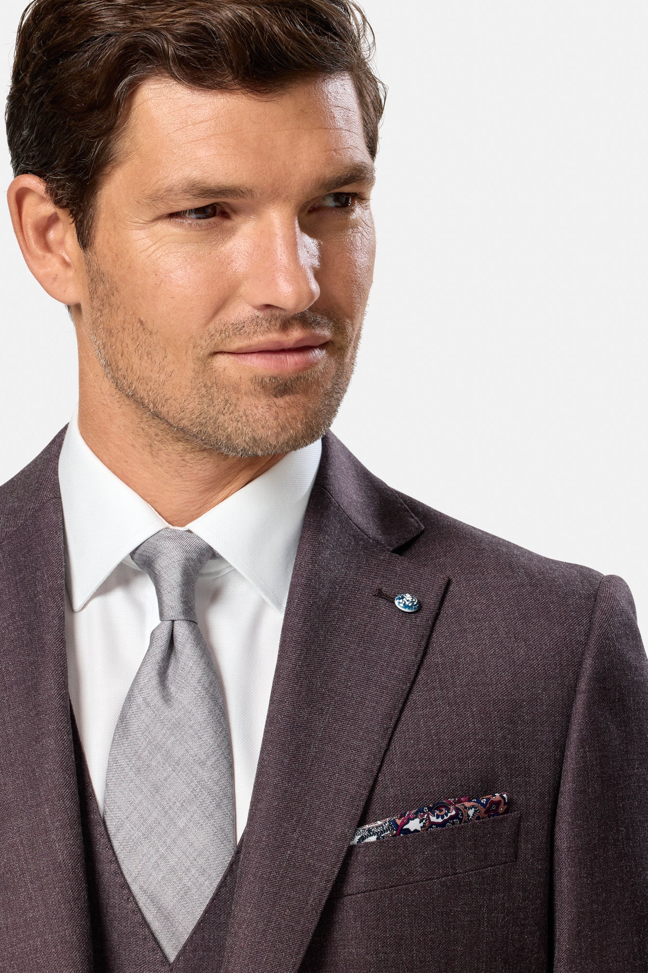 Man wearing a grape  suit with a gray tie and floral pocket square on a white background