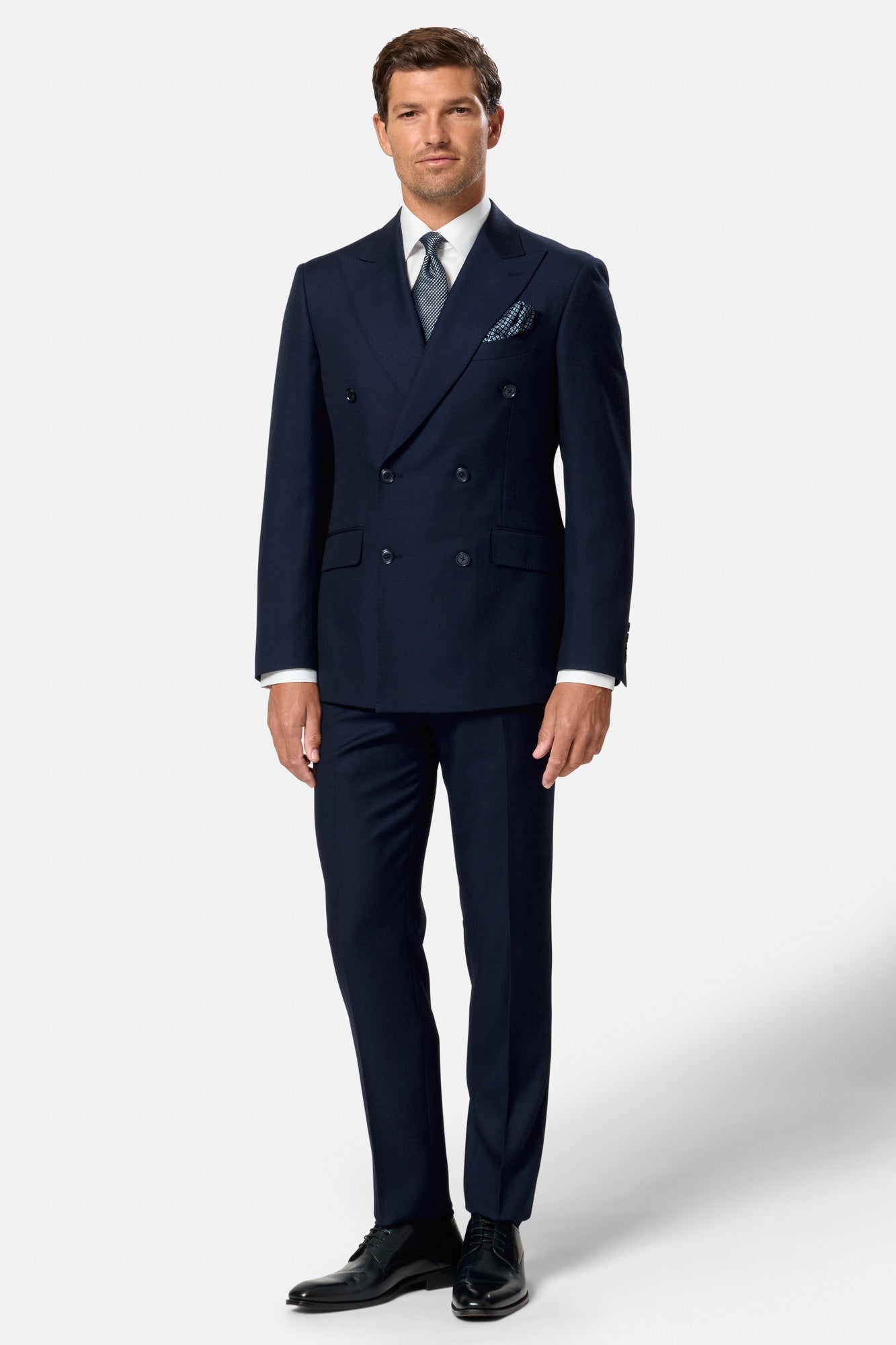 Man wearing a navy indigo double breasted suit with a white shirt and black shoes on a light gray background
