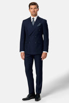 Man wearing a navy indigo double breasted suit with a white shirt and black shoes on a light gray background