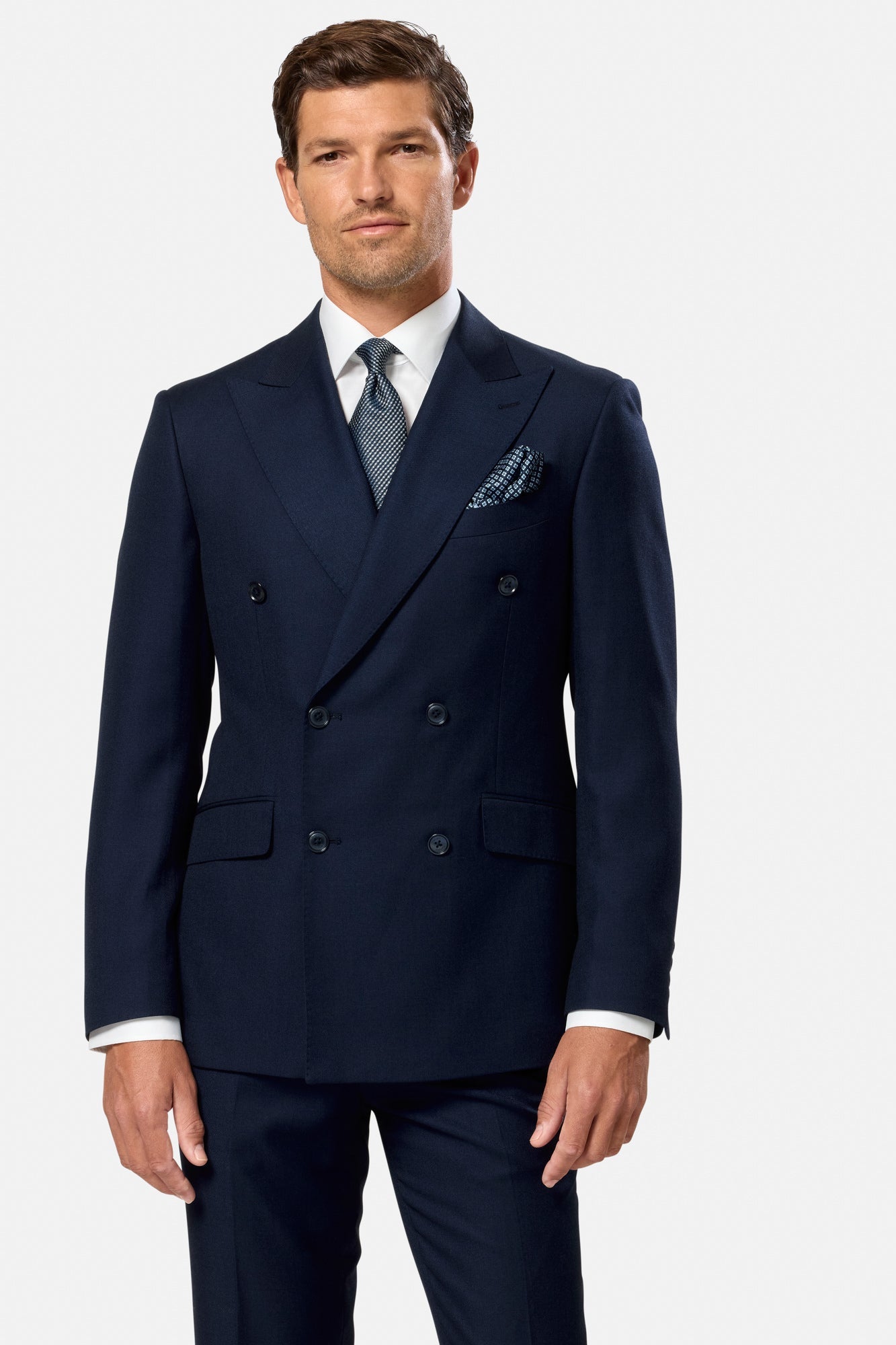 Man wearing a navy blue indigo double breasted suit with a white shirt and patterned tie on a light gray background
