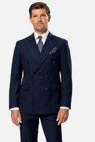Man wearing a navy blue indigo double breasted suit with a white shirt and patterned tie on a light gray background