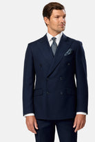 Man wearing a navy indigo double breasted  suit with a white shirt and patterned tie on a light gray background