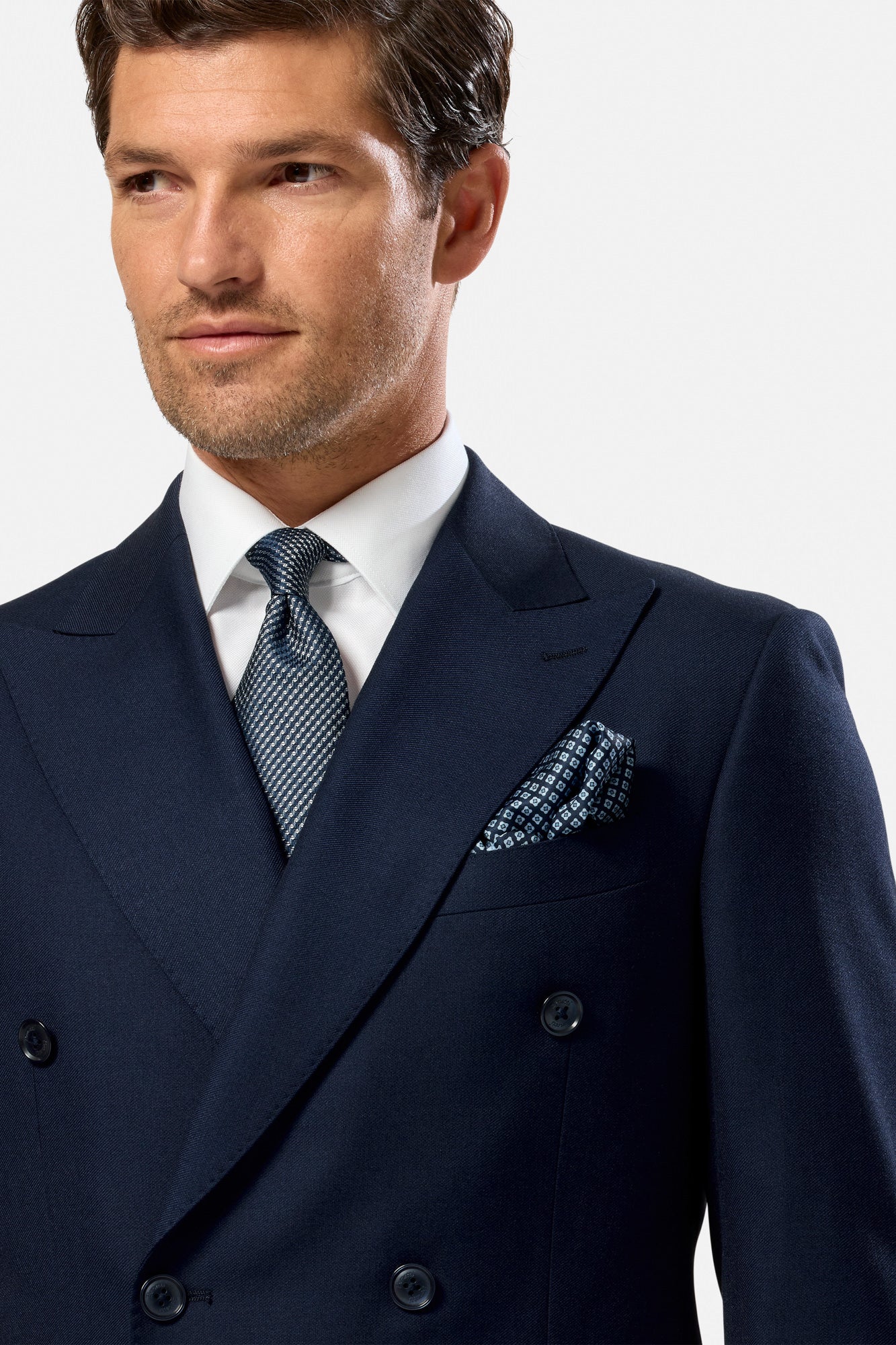Man wearing a navy double-breasted suit with a white shirt and patterned tie on a light gray background