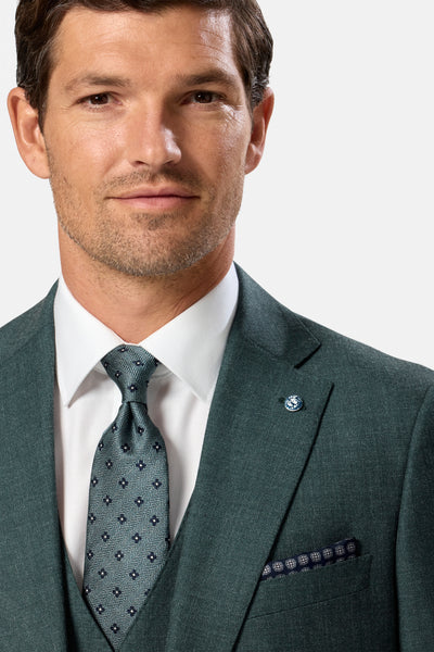 Man wearing a green suit with a patterned tie on a light gray background