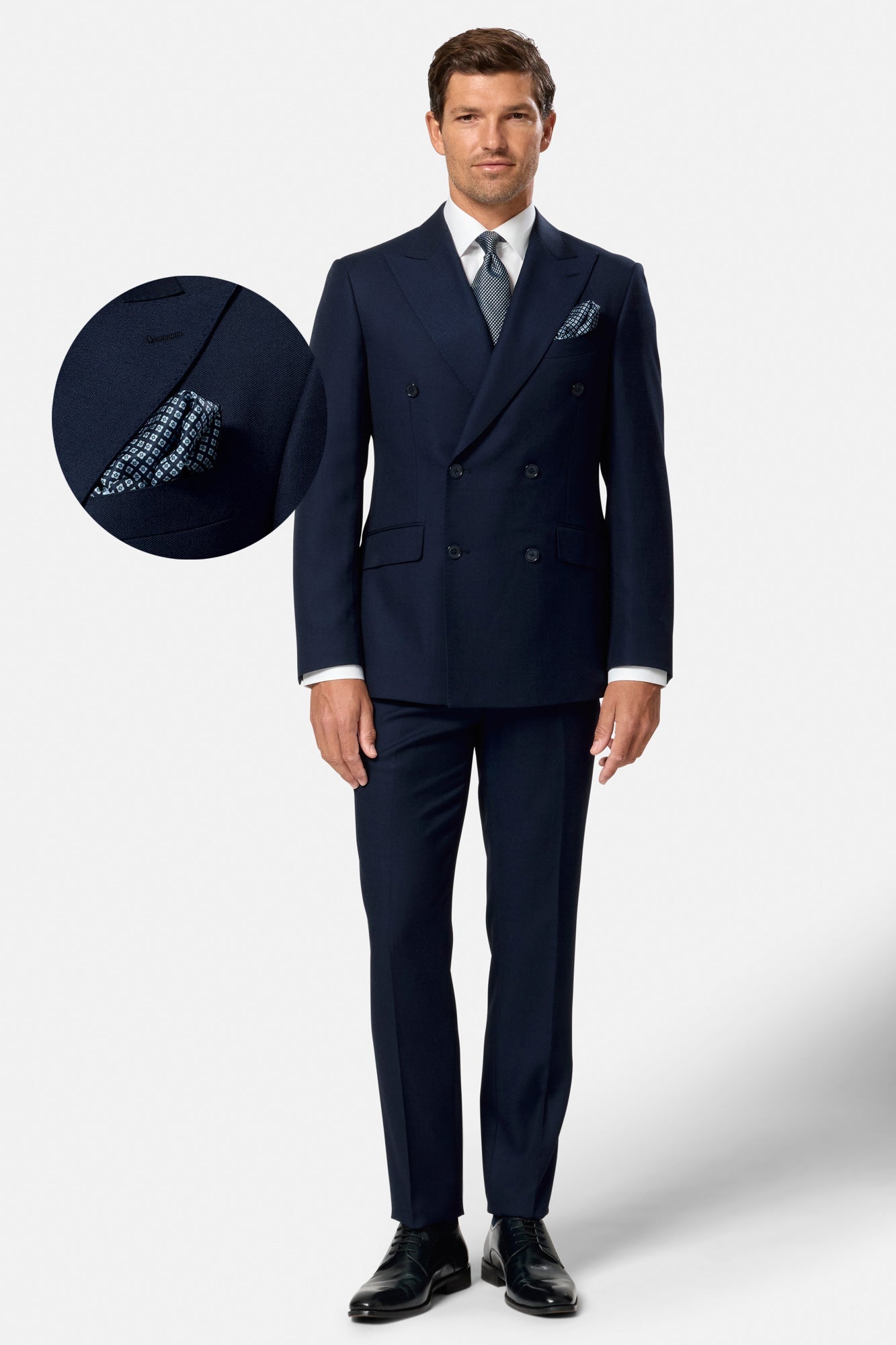 Man wearing a navy indigo double breasted suit with a white shirt and black shoes on a white background