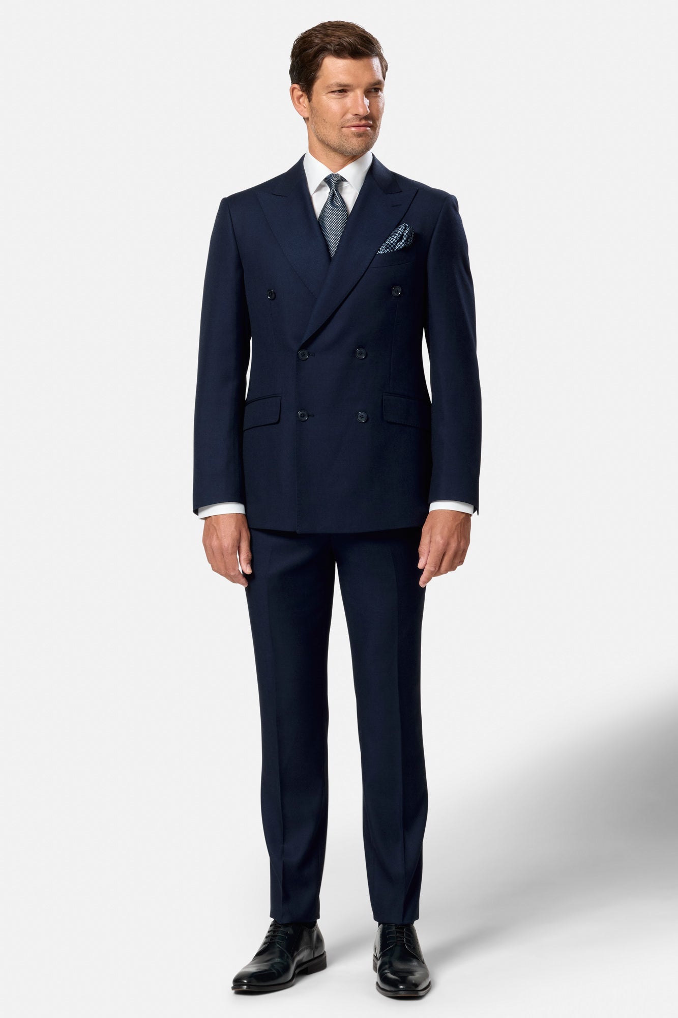 Man wearing a navy blue indigo double breasted suit with a white shirt and black shoes on a white background