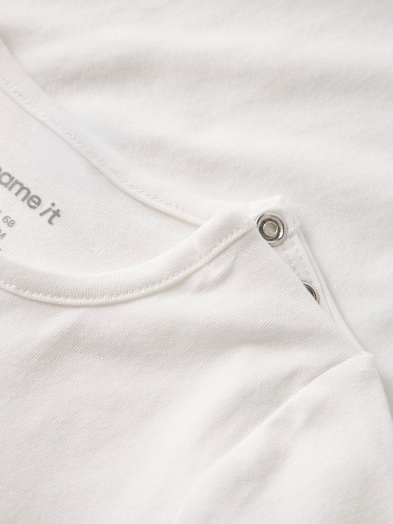 Close-up of a white baby outfit with a collar and button detail, featuring the brand 'Name it'.
