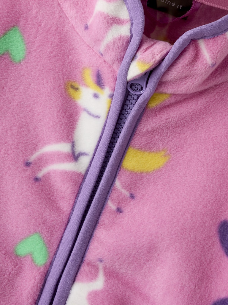 Close-up of a purple zipper on a pink fabric with heart and unicorn patterns.