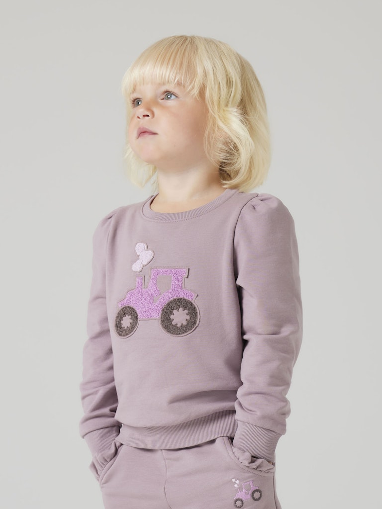 Child wearing a light purple sweatshirt with a decorative design on a plain background