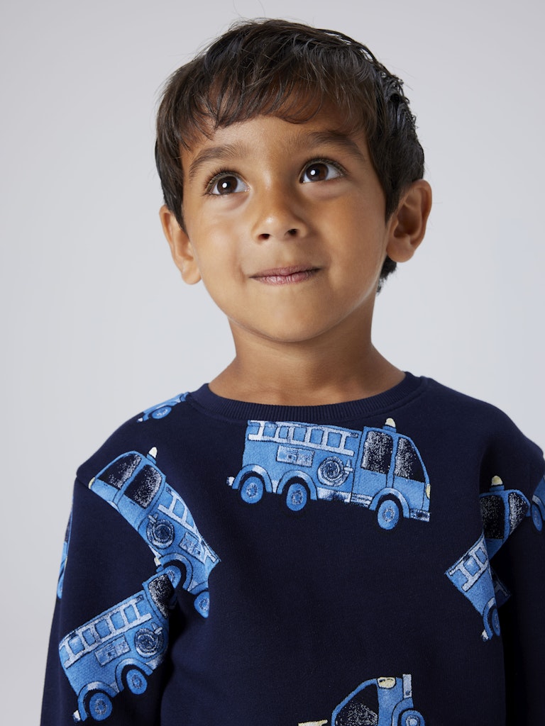 Child wearing a navy blue sweater with blue truck patterns on a plain background