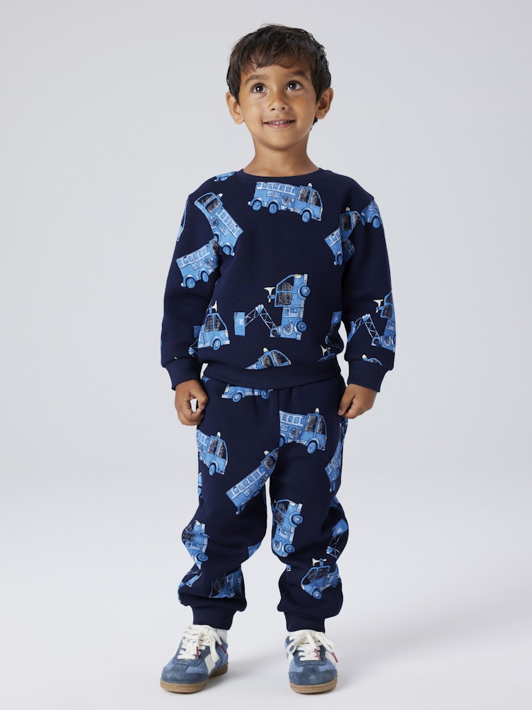 Child wearing a navy blue outfit with blue truck patterns on a white background