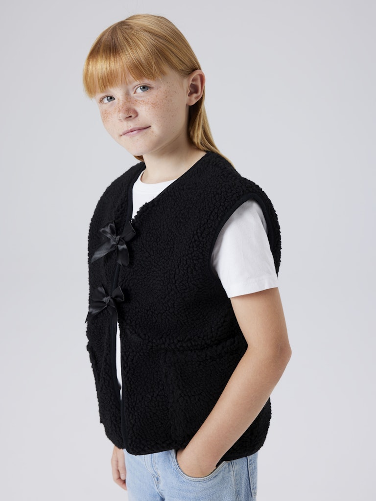 Young girl wearing a black vest with bow details on a plain background