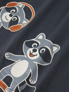 Close-up of a navy blue fabric garment featuring a cartoon raccoon print in gray, white, black, and orange.