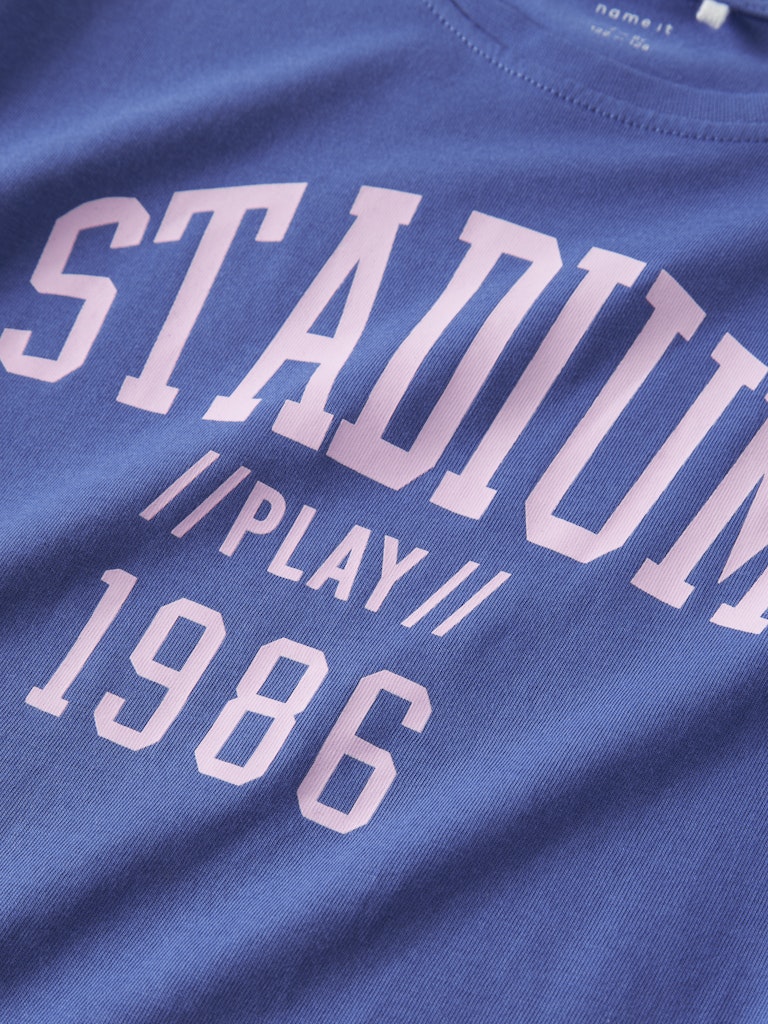 Blue t-shirt with 'STADIUM // PLAY // 1986' text in white