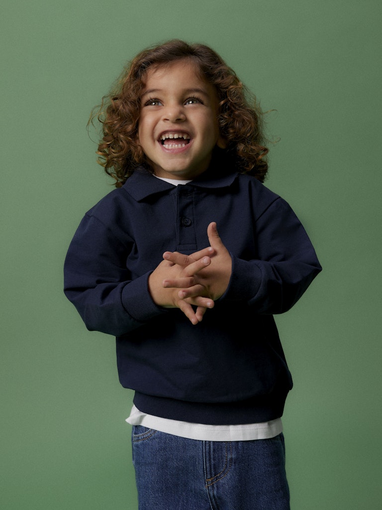 Child wearing a navy blue sweater over a white shirt, standing against a green background