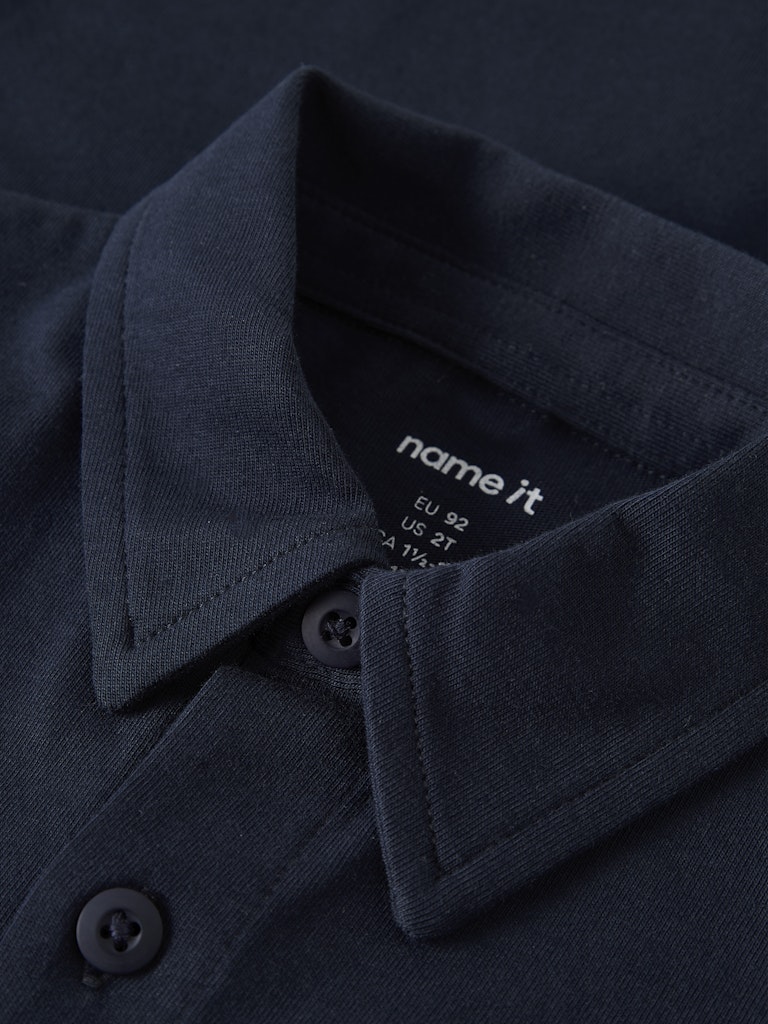 Close-up of a navy shirt collar with 'name it' label on a dark background