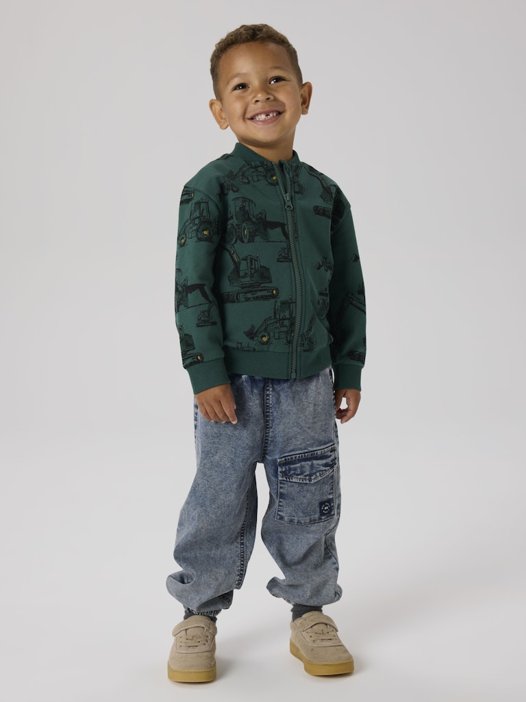 Child wearing a green jacket with a pattern and blue jeans on a white background