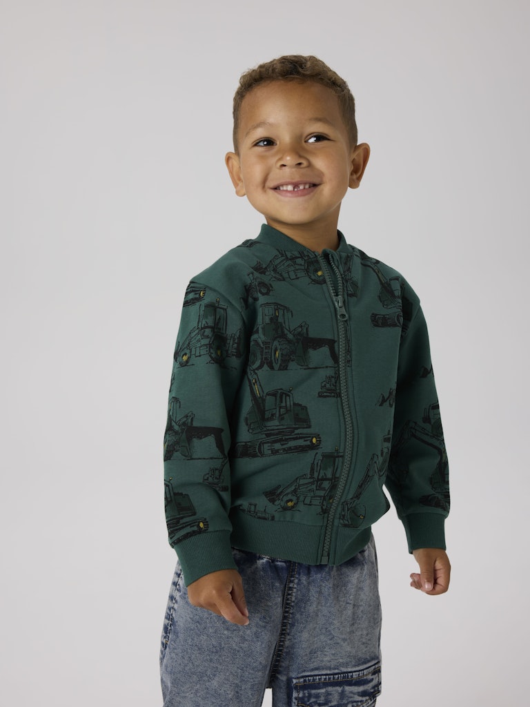 Child wearing a green jacket with vehicle patterns on a plain background