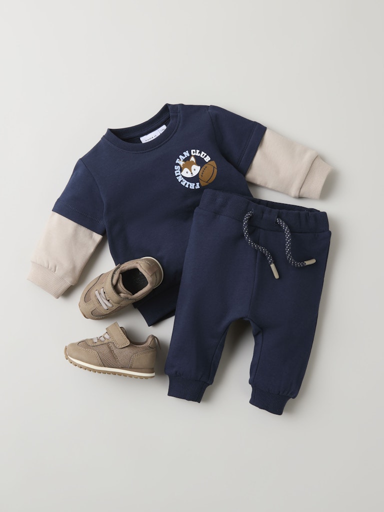 Navy blue children's outfit with beige sleeves and brown shoes on a light gray background