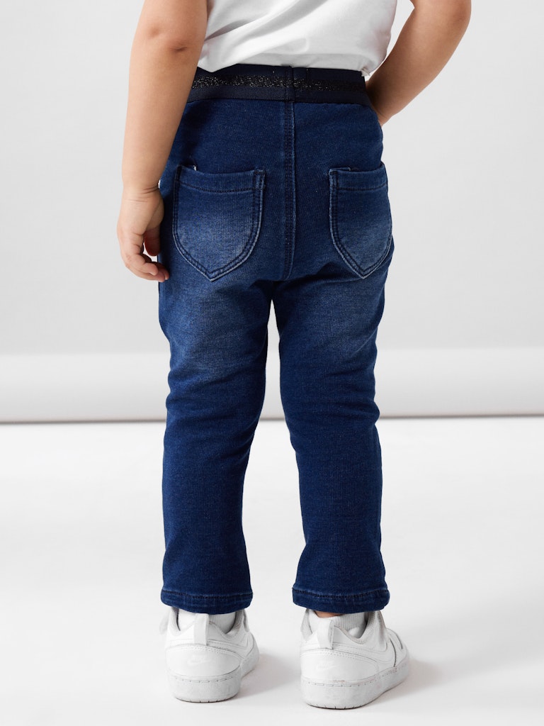 Child wearing blue jeans and white sneakers on a light gray background