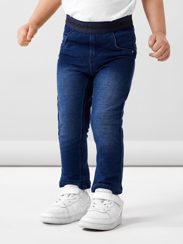 Child wearing blue jeans and white sneakers on a light gray background