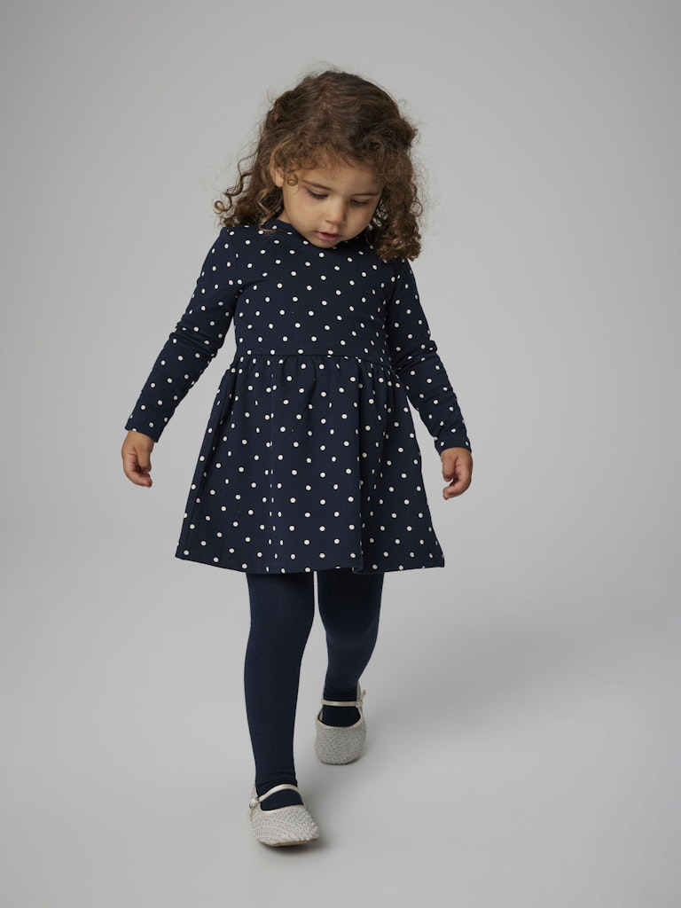 Child wearing a navy dress with white polka dots on a plain background