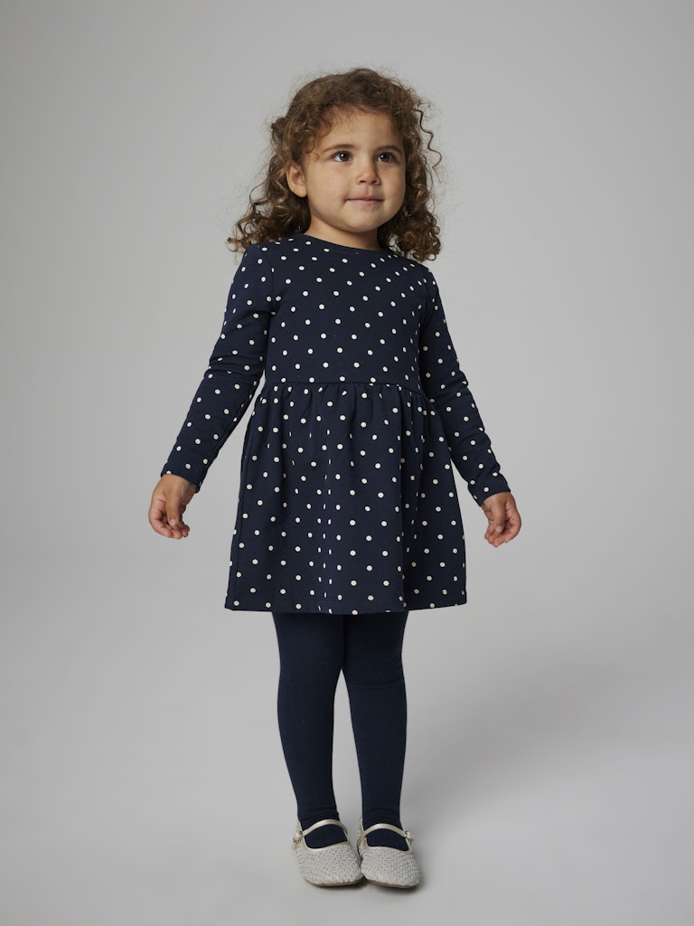 Child wearing a navy dress with white polka dots on a plain background