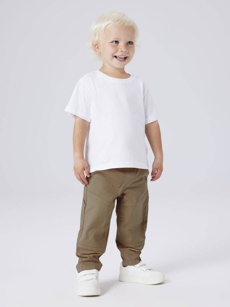 Child wearing a white t-shirt and brown pants on a light gray background