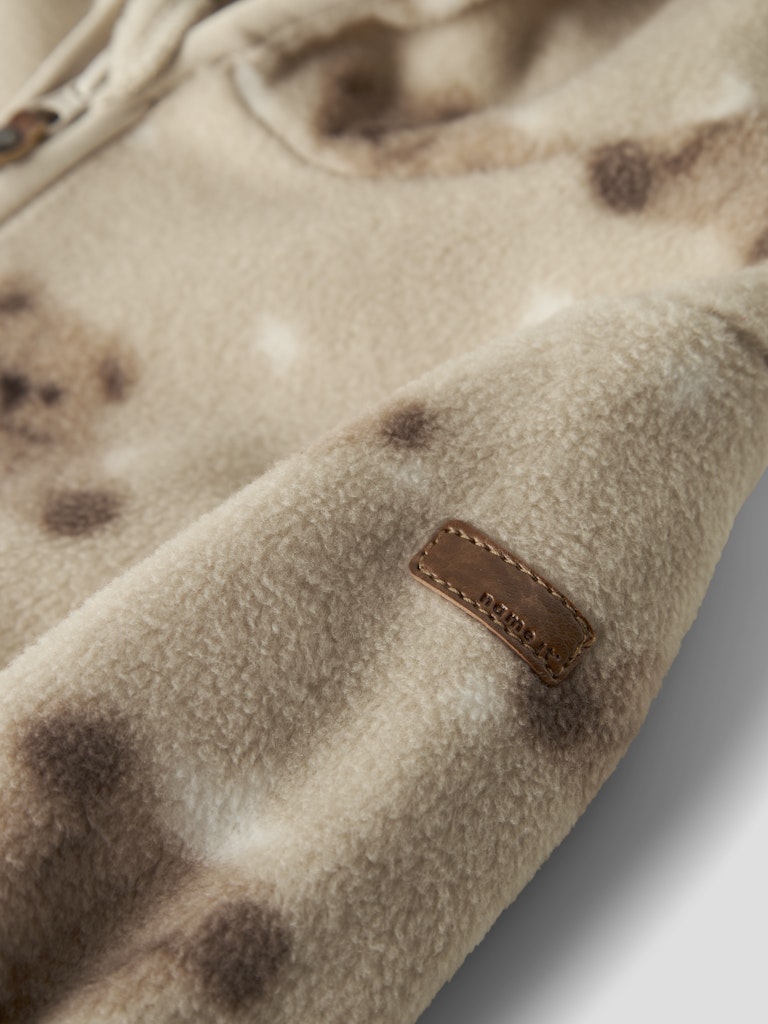 Close-up of a beige fleece onesie with brown spots and a brand label.
