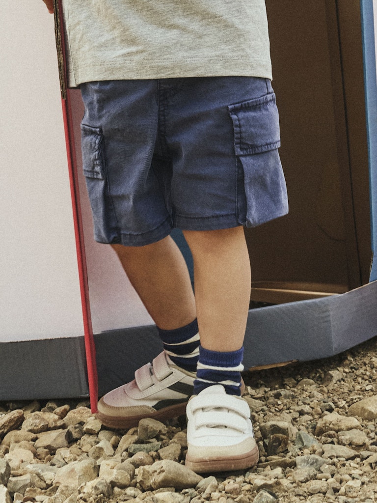 Child wearing navy blue shorts and white sneakers on a rocky ground.