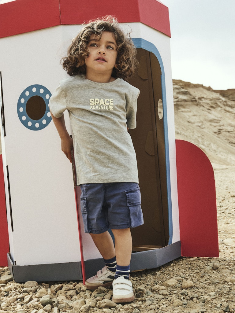 Child standing next to a toy space ship in an outdoor setting