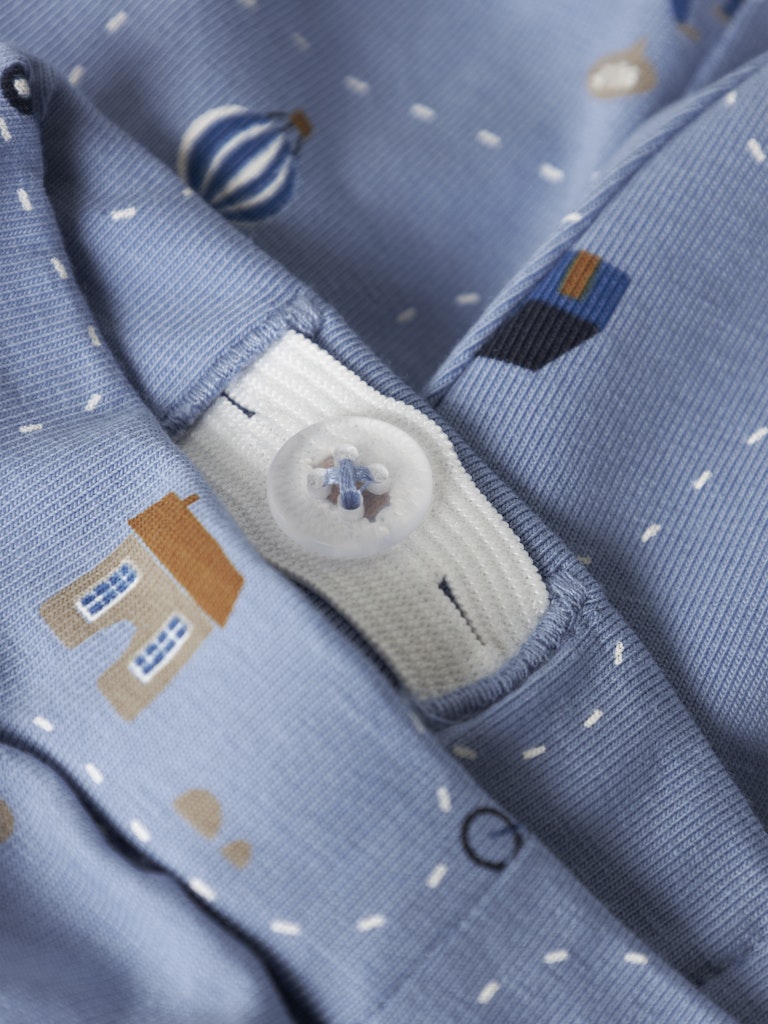 Close-up of a blue fabric with cartoon designs and a button, featuring small balloons and houses.