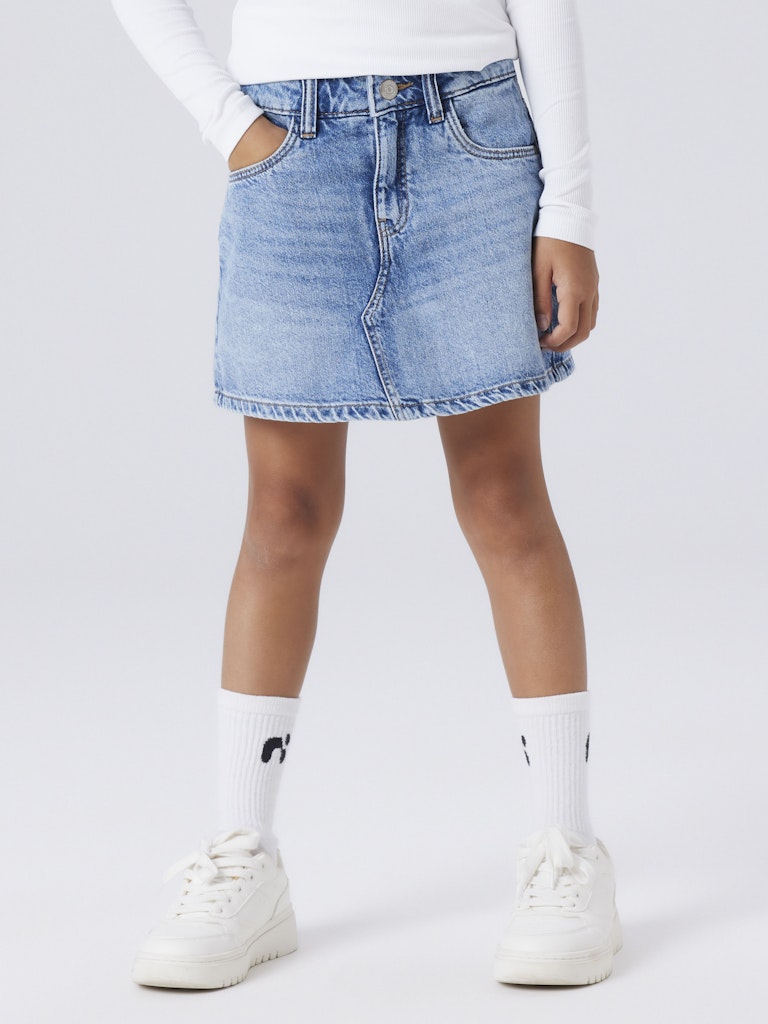 Person wearing a blue denim skort with white sneakers and socks on a light gray background