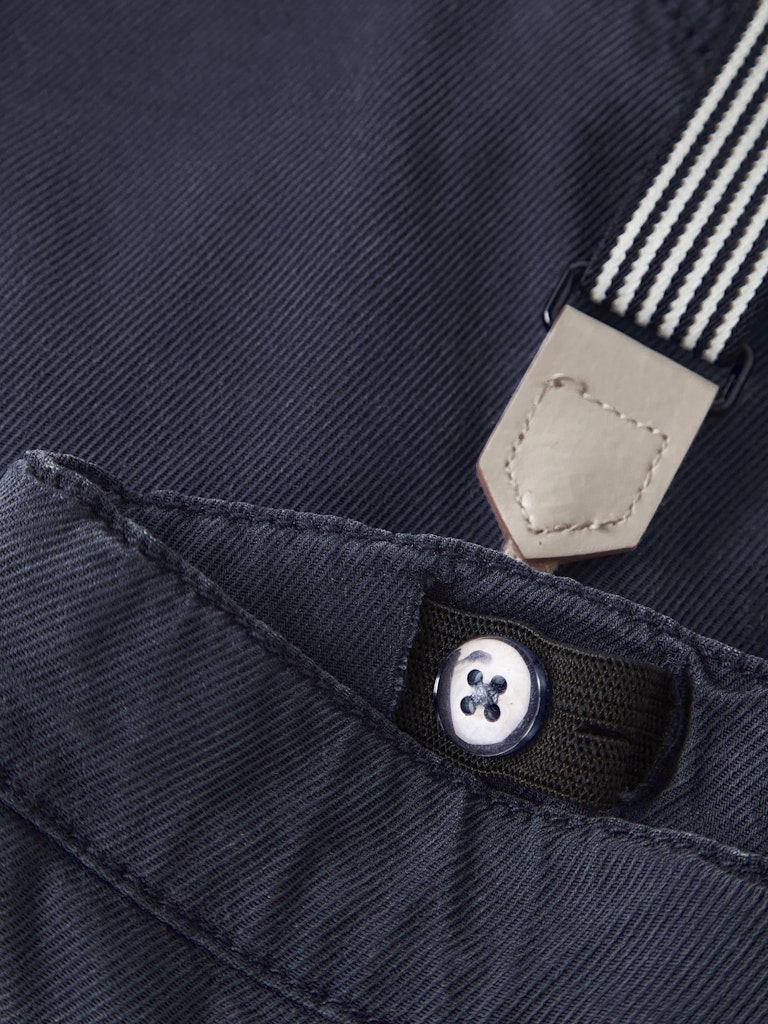Close-up of a button on dark blue fabric with a beige strap featuring white stripes.