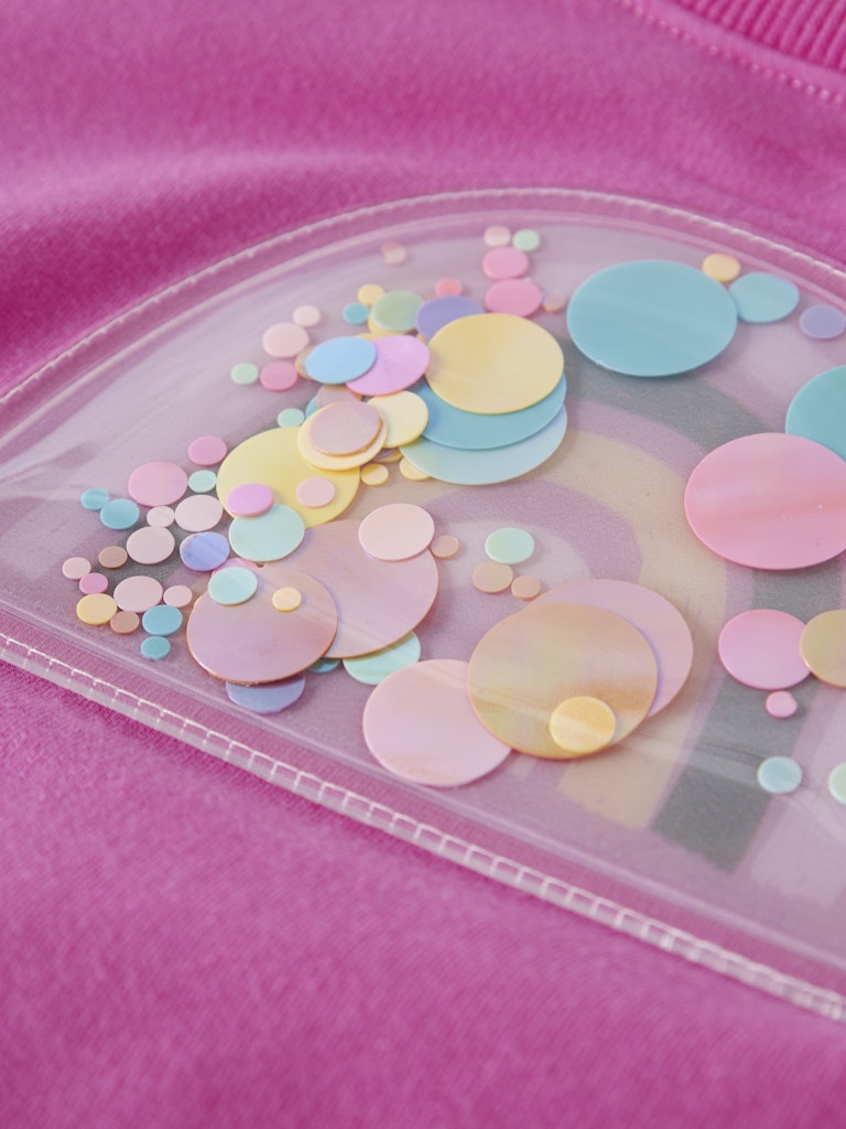 Pastel-colored round confetti in a clear container on a pink background
