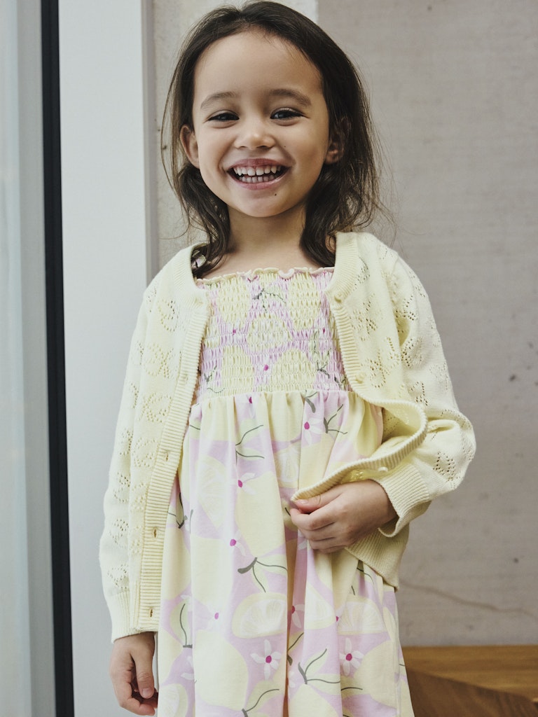Child wearing a yellow dress with floral patterns and a matching cardigan indoors.