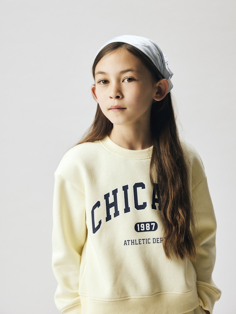 Child wearing a beige sweatshirt with 'Chicago 1987' text on a plain background