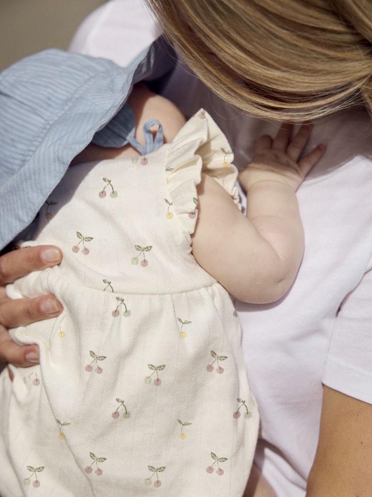 Baby in a cream dress with cherry pattern held by an adult