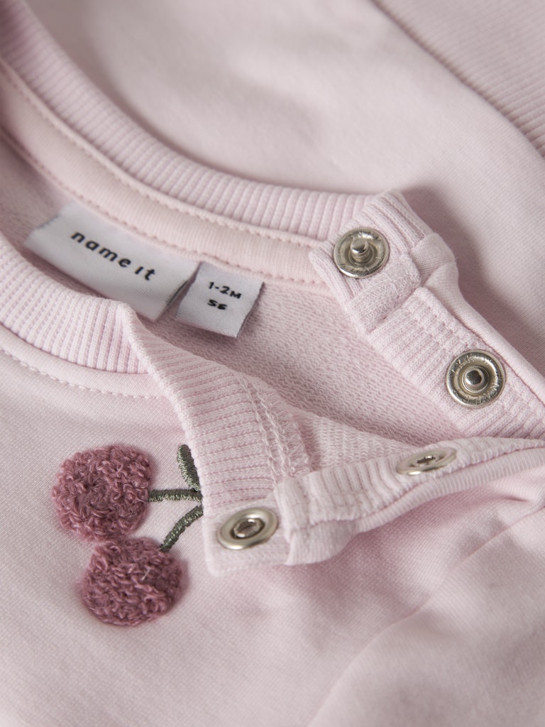 Close-up of a pink baby outfit with buttons and a 'name it' label.