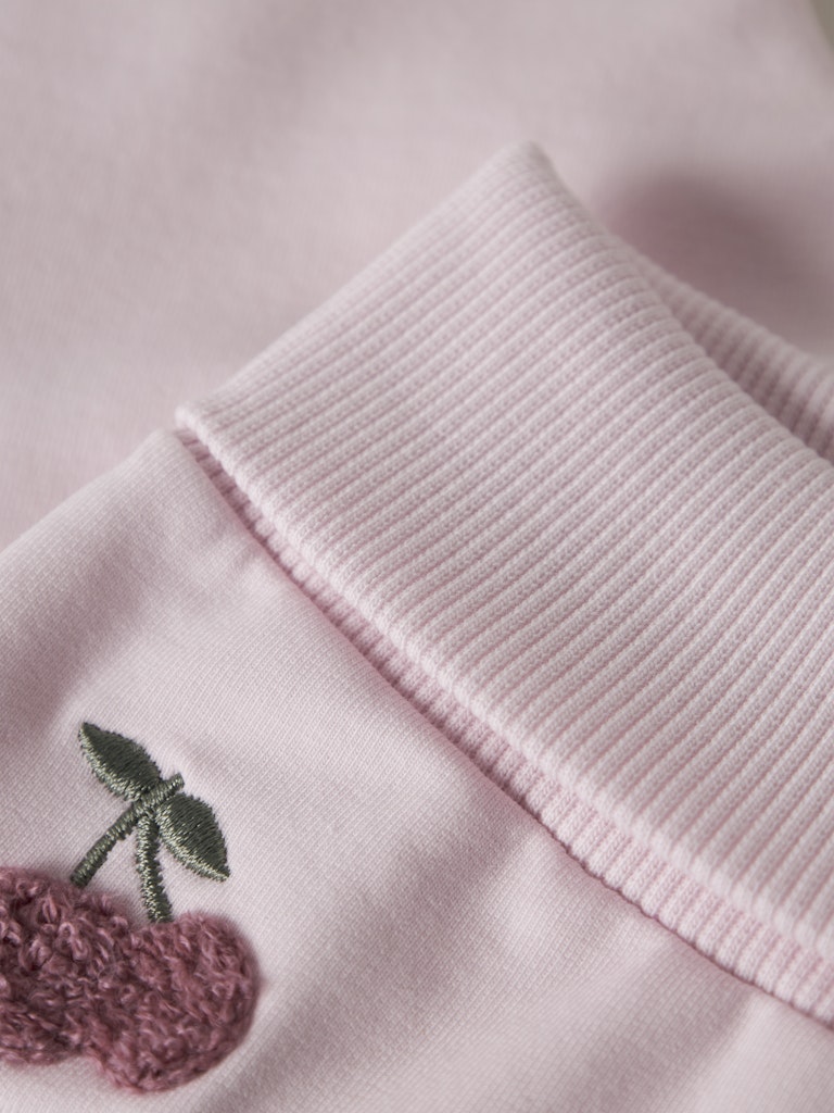 Close-up of a pink garment with embroidered cherries on a light pink background