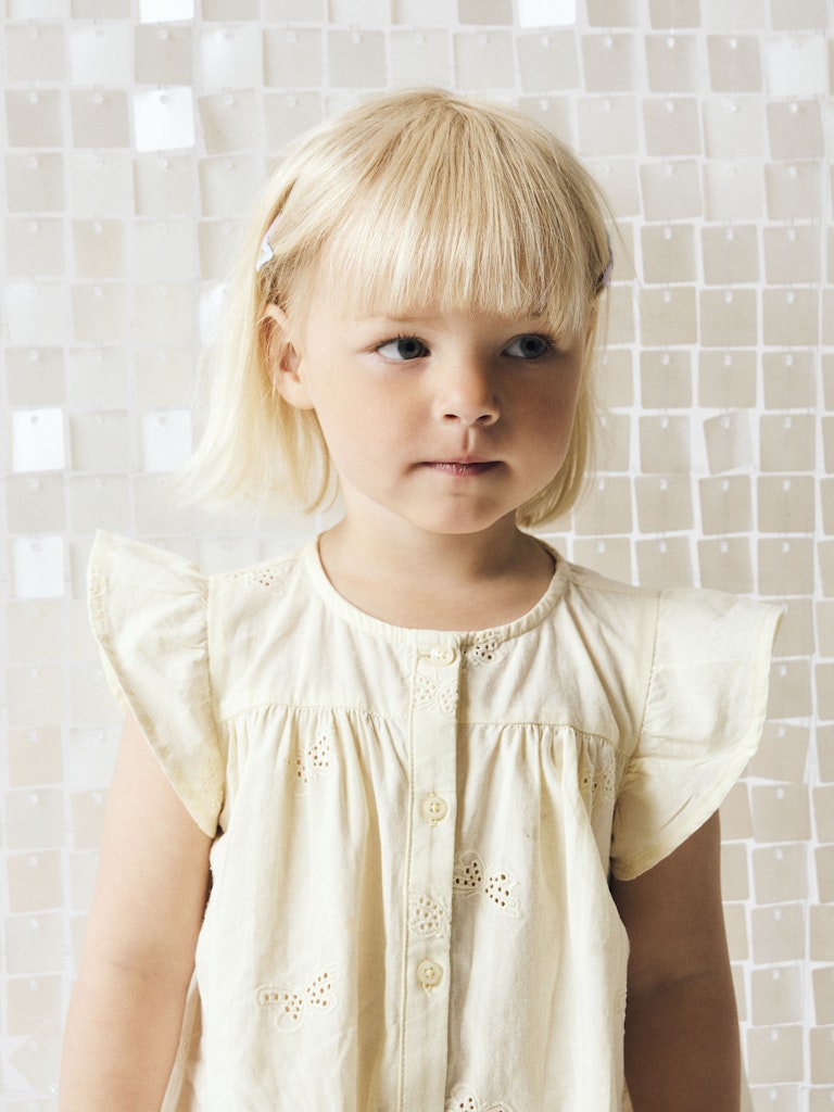 Young girl wearing a light-colored blouse against a tiled wall.