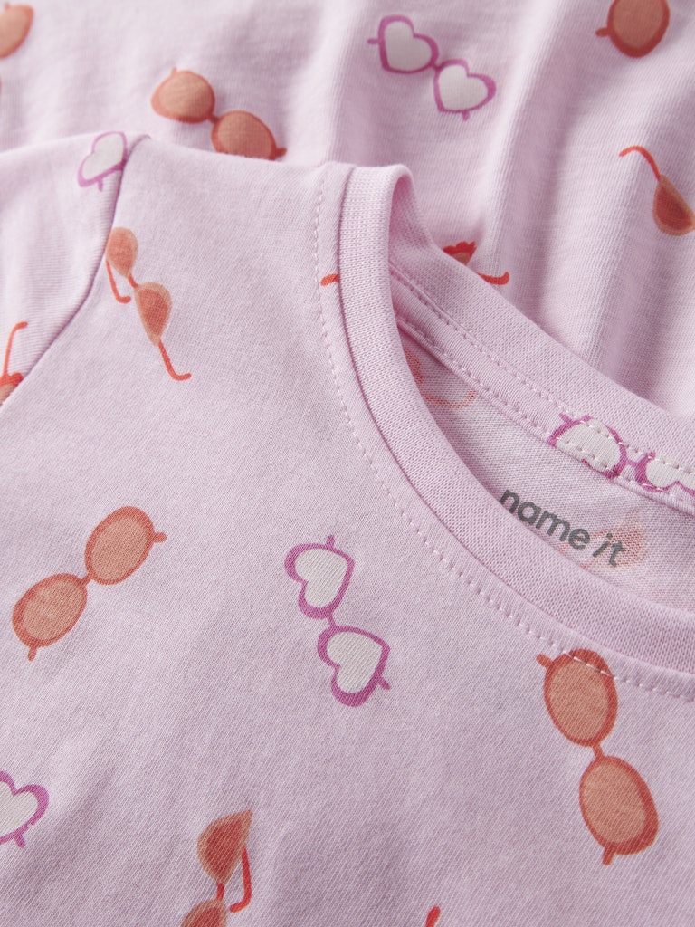 Close-up of a baby outfit with sunglasses and heart patterns on a light pink background.