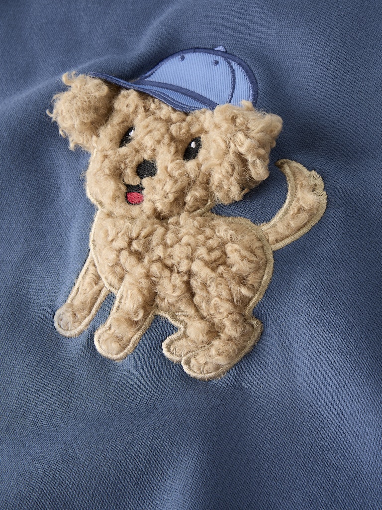 Embroidered dog patch with a blue cap on a blue fabric background