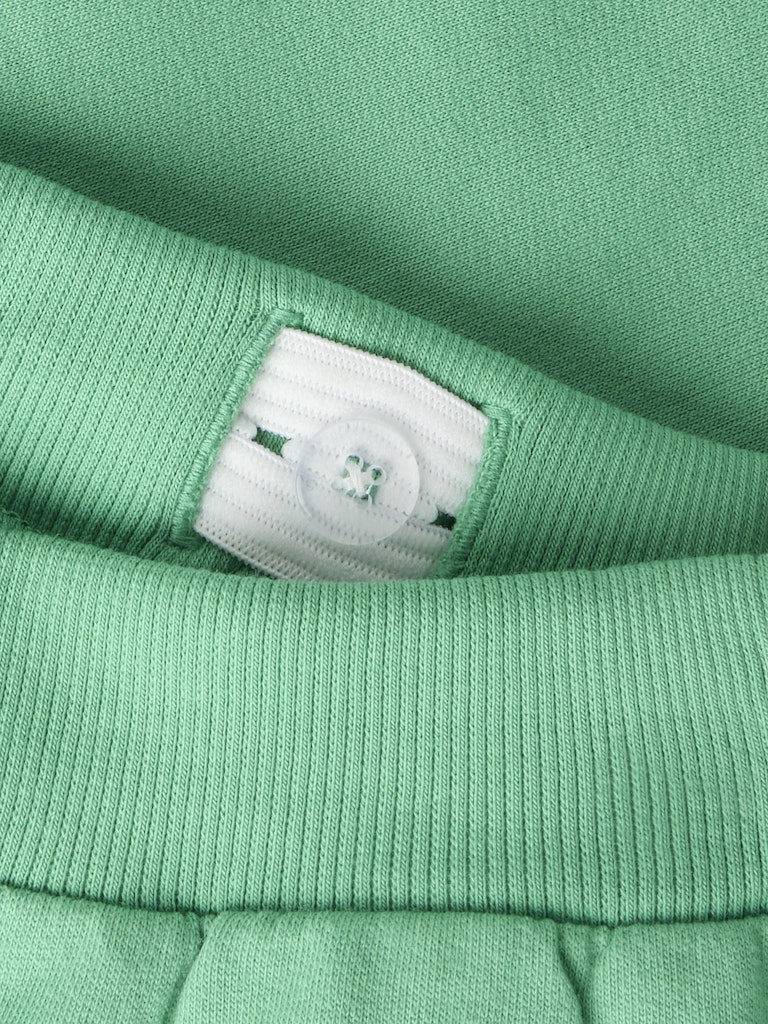 Close-up of green sweatpants with a button adjustable waist.