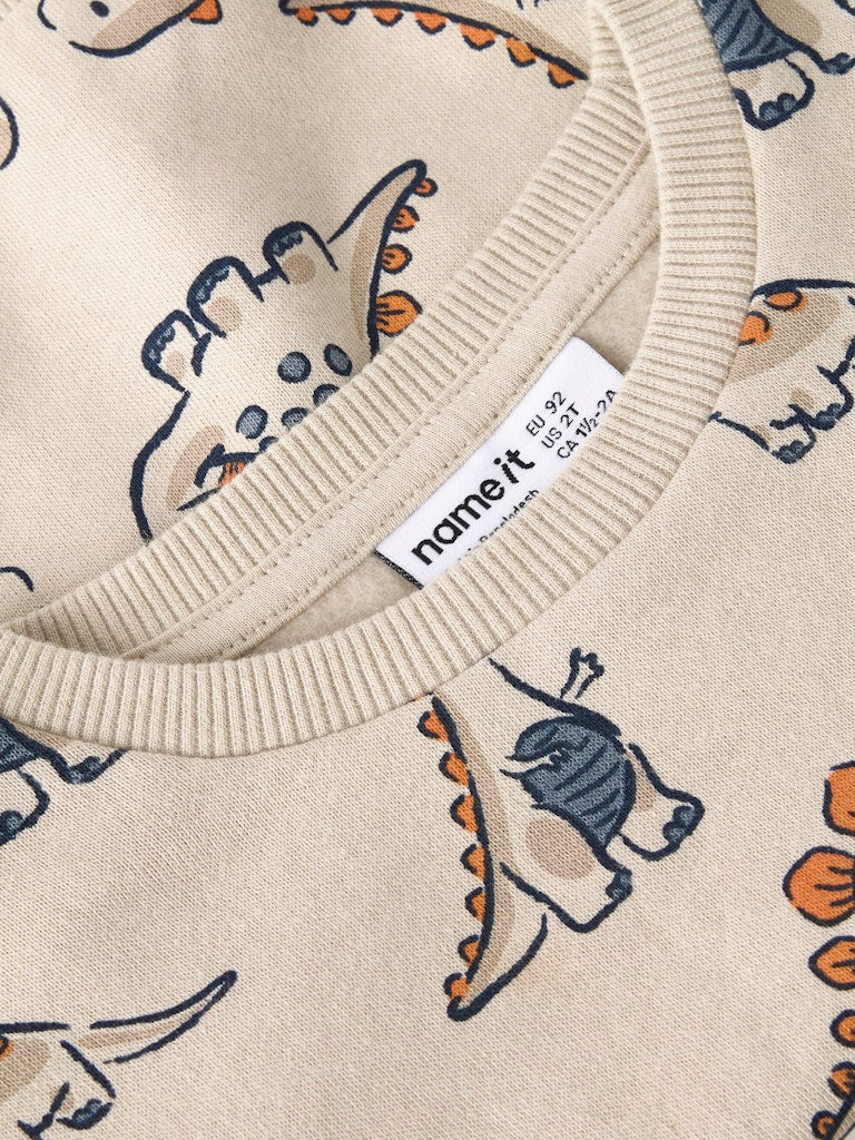 Close-up of a beige sweater with dinosaur pattern and 'noneit' label.
