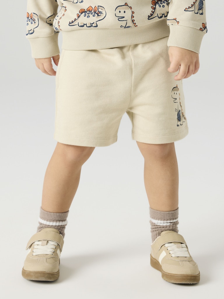Child wearing a beige outfit with dinosaur patterns on a white background